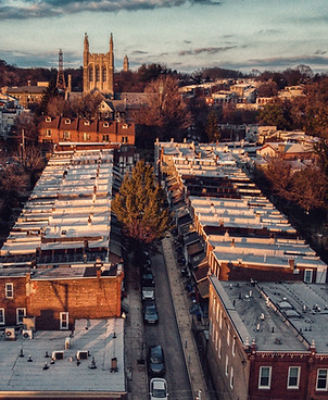 Image shows an arial view of a west Philly street, showing the roofs of rowhomes with an eye-catching stone church in the background. Photo credit: Edan Cohen